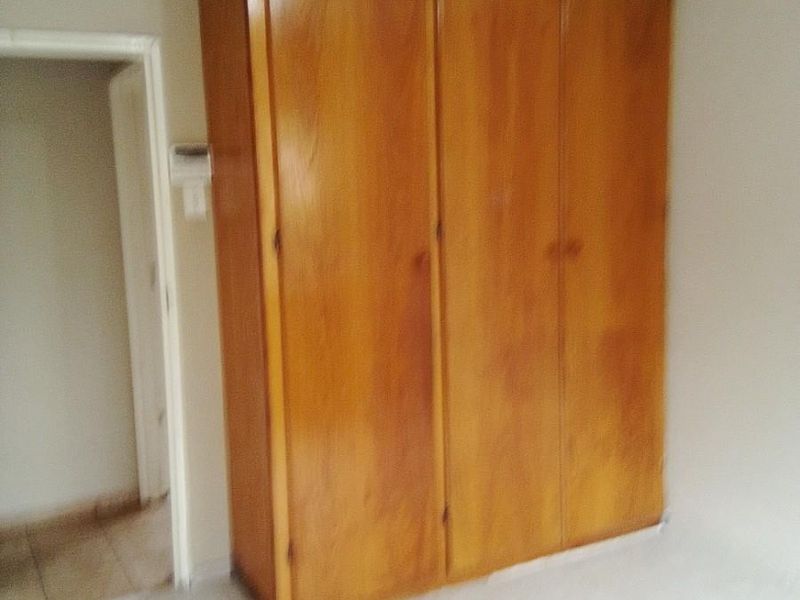 A bedroom featuring a large built-in wooden wardrobe and tiled flooring, offering a clean and functional space.