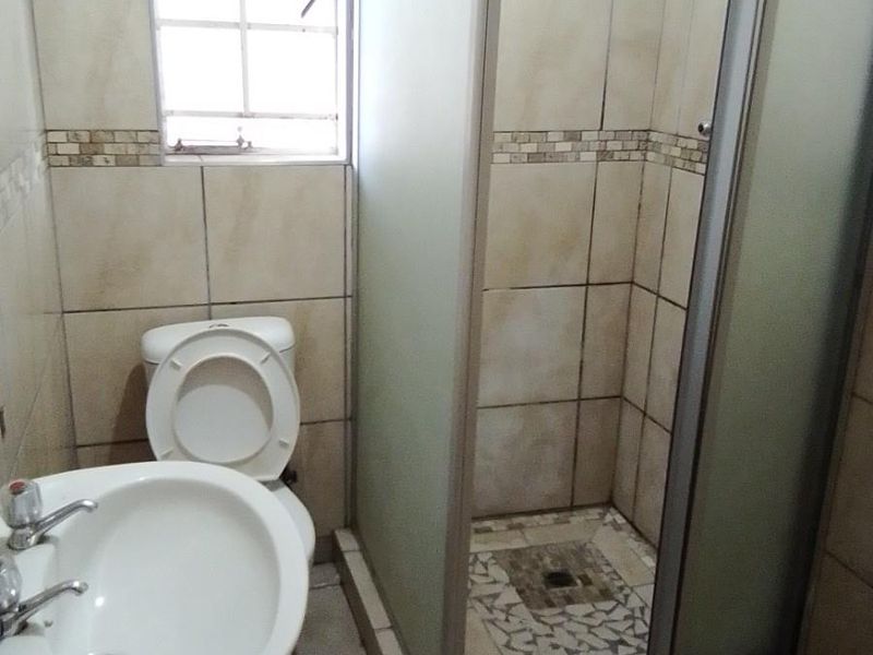 A functional bathroom featuring a pedestal basin, toilet, and a glass-enclosed shower with tiled walls and flooring.