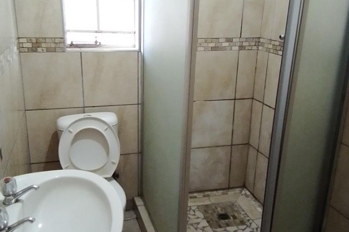 A functional bathroom featuring a pedestal basin, toilet, and a glass-enclosed shower with tiled walls and flooring.