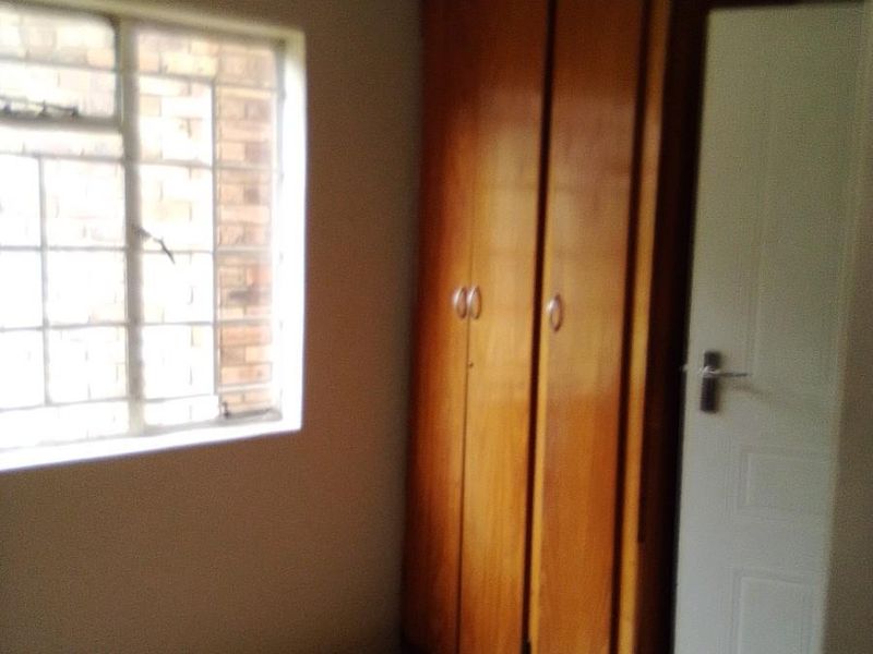 A simple bedroom featuring tiled flooring, a built-in wooden wardrobe, and a steel-framed window.