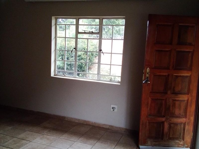 An empty bedroom featuring tiled flooring, a ceiling fan, and a wooden panel door, offering a blank canvas for personalization.