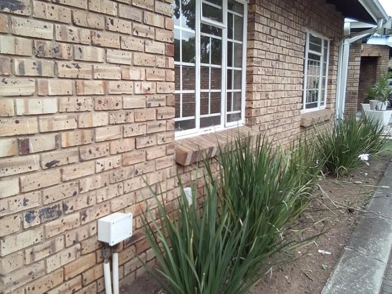 Side view of a face brick townhouse exterior featuring steel frame windows, guttering, and a small garden bed with concrete kerbing.