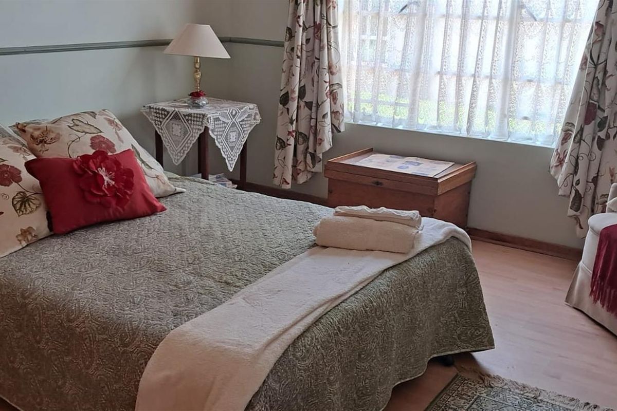 A cozy bedroom featuring laminate flooring, a dado rail, and a large window allowing for natural light.