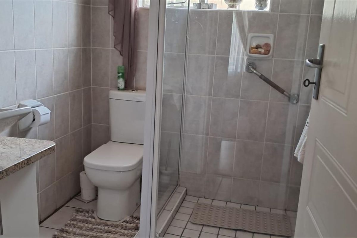 A functional bathroom featuring a glass-enclosed shower with grab rail, a vanity with a vessel sink, and tiled walls and flooring.