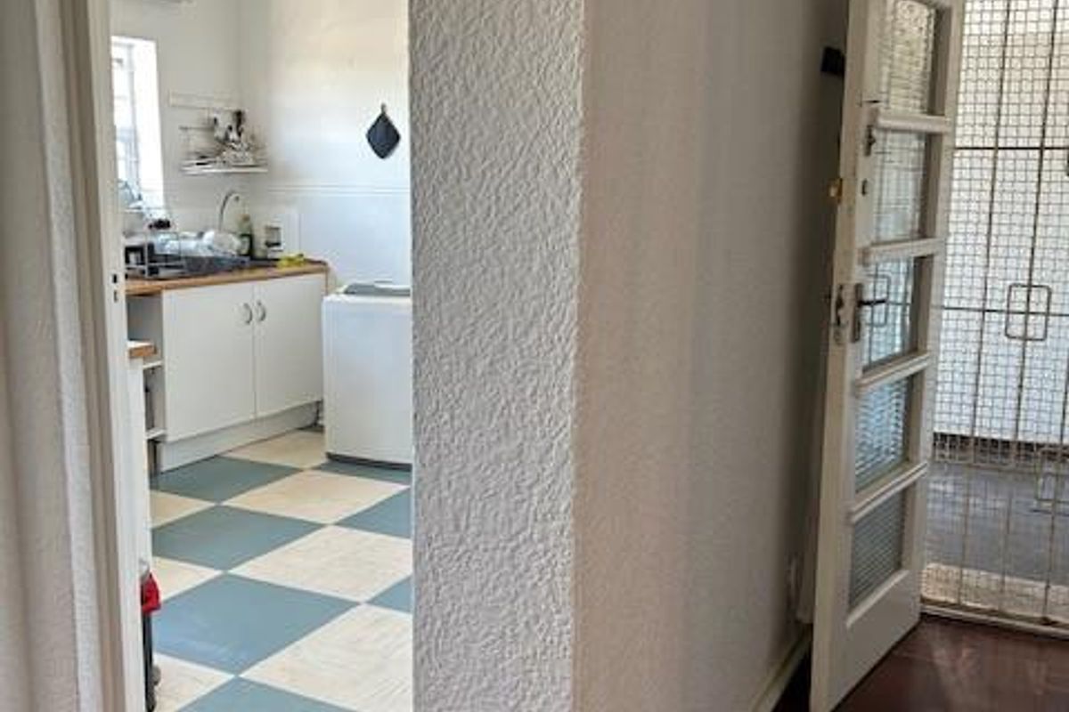 View from a hallway into a kitchen area featuring checkerboard flooring, white cabinetry, and a security gate at the entrance.