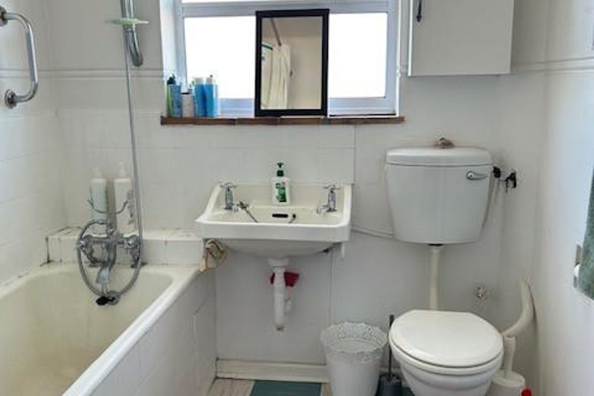 A dated bathroom featuring a standard bathtub with shower attachment, wall-mounted basin, and toilet, requiring modernization of finishes and fixtures.