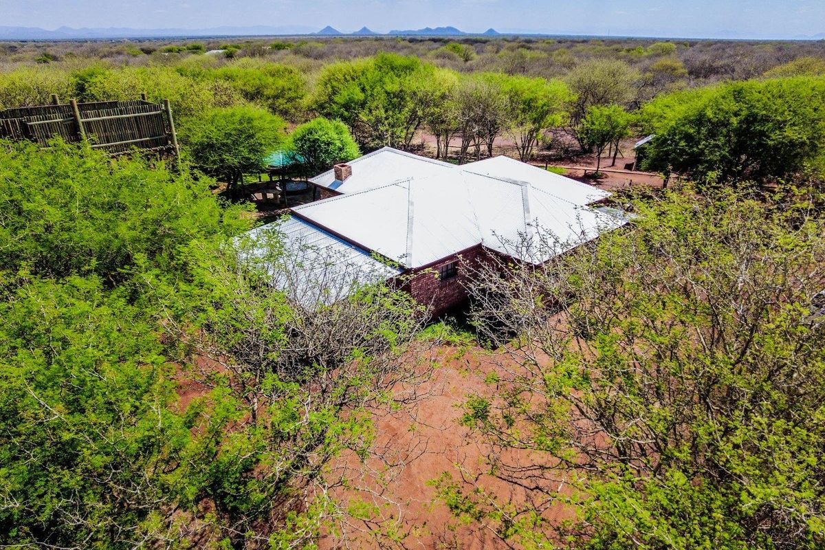 Aerial view of a farm property featuring a brick dwelling with a metal roof, surrounded by natural bushveld and an elevated wooden viewing deck.