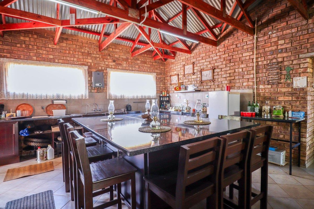 Rustic kitchen featuring exposed brick walls, timber roof trusses, and a large central granite island, offering a warm and functional farm-style cooking space.