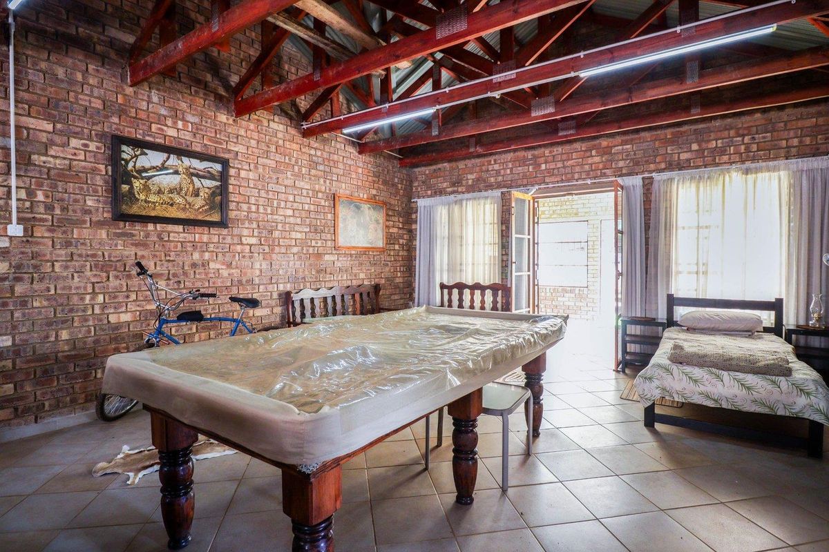Spacious living area featuring rustic facebrick walls, exposed timber roof trusses, and tiled flooring with direct access to the outdoors.