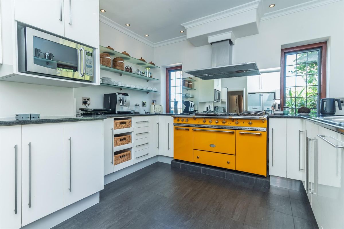 Modern kitchen featuring white cabinetry, dark tiled flooring, glass shelving, and a prominent yellow professional-style range cooker with an overhead extractor fan.