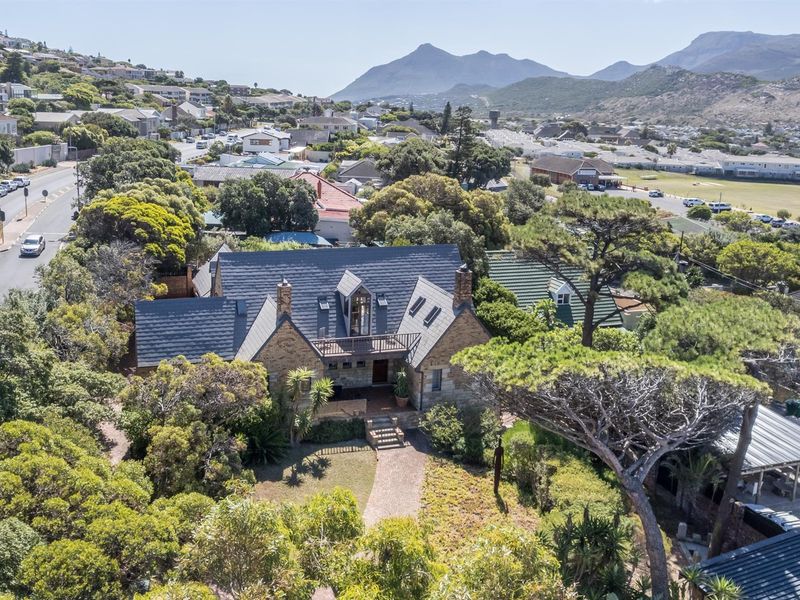 Aerial view of a stone-clad residence featuring a pitched slate roof, dormer windows, and a balcony, set within a lush, tree-filled garden.
