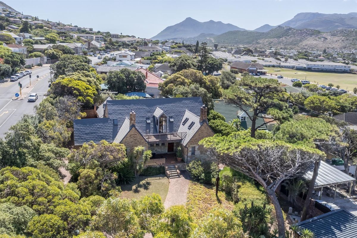 Aerial view of a stone-clad residence featuring a pitched slate roof, dormer windows, and a balcony, set within a lush, tree-filled garden.