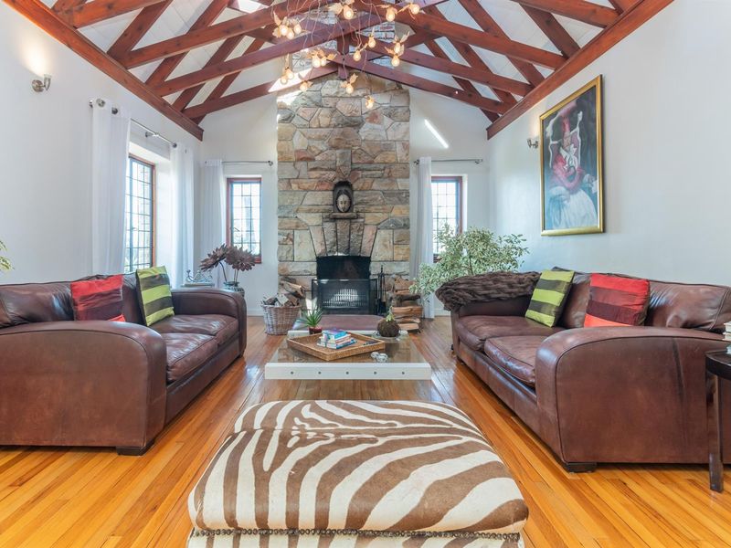 Spacious living room featuring a vaulted timber-beamed ceiling, polished hardwood flooring, and a prominent floor-to-ceiling stone fireplace as the central focal point.