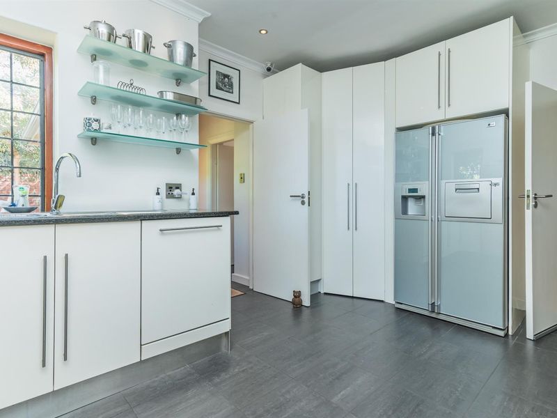 A modern kitchen featuring white cabinetry, dark stone countertops, glass shelving, and integrated appliance space with dark tiled flooring.