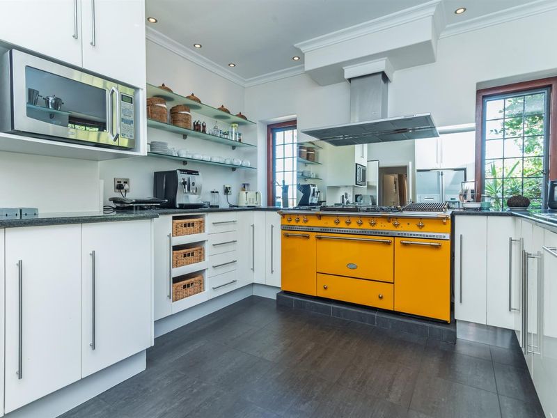 Modern kitchen featuring white cabinetry, dark tiled flooring, glass shelving, and a prominent yellow professional-style range cooker with an overhead extractor fan.