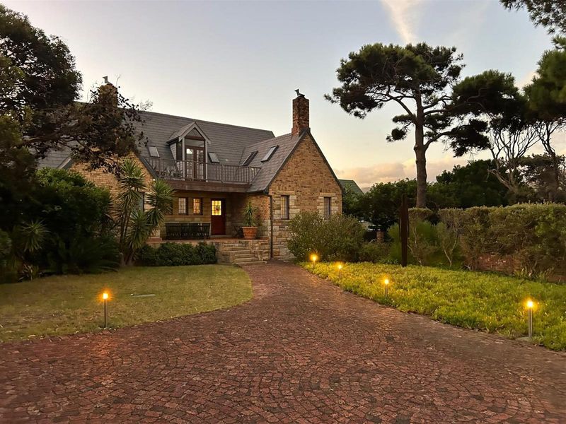 Charming stone-clad residence featuring a slate roof, upper-level balcony, and a beautifully landscaped front garden with a paved driveway and ambient lighting.