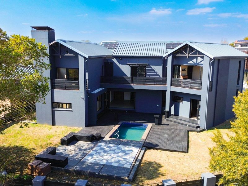 Aerial view of the rear elevation featuring a modern two-story home with a swimming pool, timber decking, and solar panels on a metal roof.