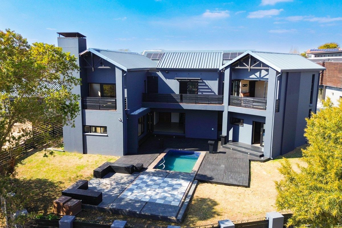 Aerial view of the rear elevation featuring a modern two-story home with a swimming pool, timber decking, and solar panels on a metal roof.