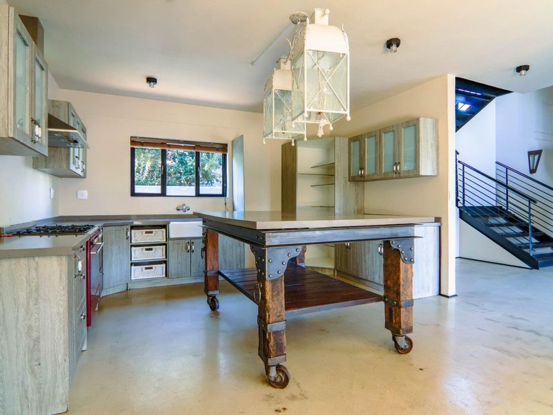 A spacious kitchen featuring industrial-style cabinetry, a large central island, farmhouse sink, and an adjacent staircase leading to the upper level.