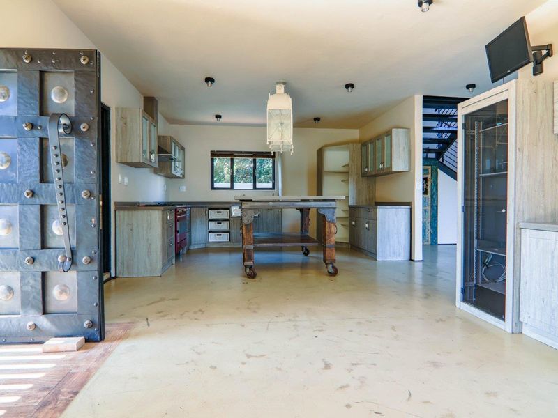A spacious kitchen featuring rustic cabinetry, a central prep island, and an industrial-style door, with an adjacent staircase leading to the upper level.