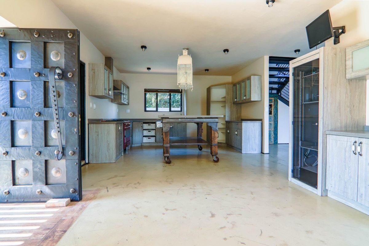 A spacious kitchen featuring rustic cabinetry, a central prep island, and an industrial-style door, with an adjacent staircase leading to the upper level.