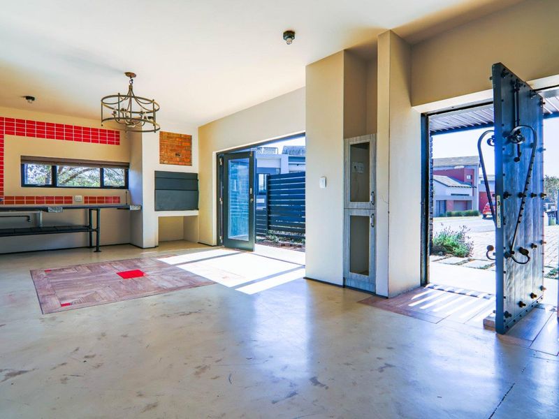 Covered patio area featuring a built-in braai, red tiled splashback, and concrete flooring, with direct access to the exterior through bi-fold doors.