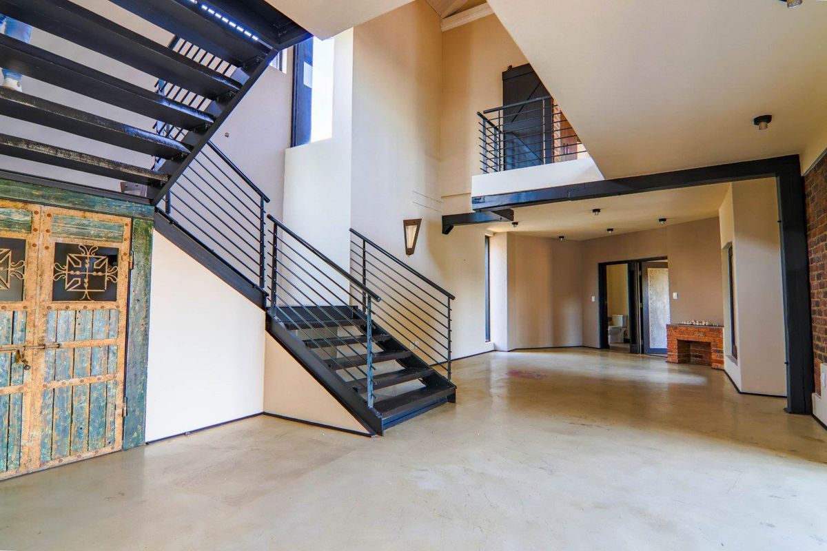 Spacious open-plan living area featuring a striking industrial metal staircase, polished concrete floors, and a mezzanine level with exposed brick accents.