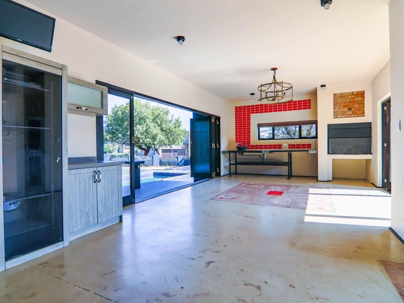 Spacious open-plan entertainment area featuring a built-in braai, red tiled splashback, and large stacking doors opening to the pool area.