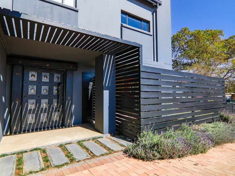 Modern front entrance featuring a striking decorative metal door, timber slat privacy screen, and a clean paved walkway leading to the porch.