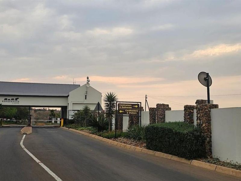 View of the secure estate entrance gate with paved access road, perimeter walling, and directional signage.