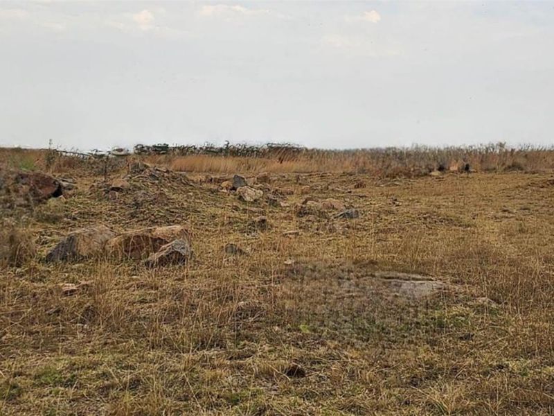 A view of the vacant residential land featuring natural terrain, dry grass, and scattered rocks.