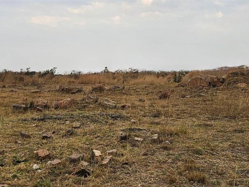 A vacant residential plot featuring natural terrain, scattered rocks, and dry vegetation, offering a blank canvas for future development.