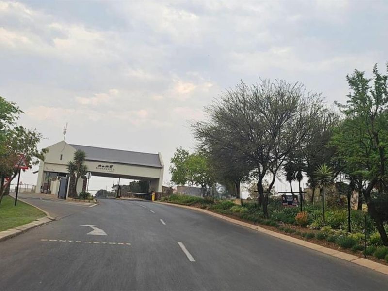 View of the secure estate entrance gate and access road, featuring landscaped verges and established trees.