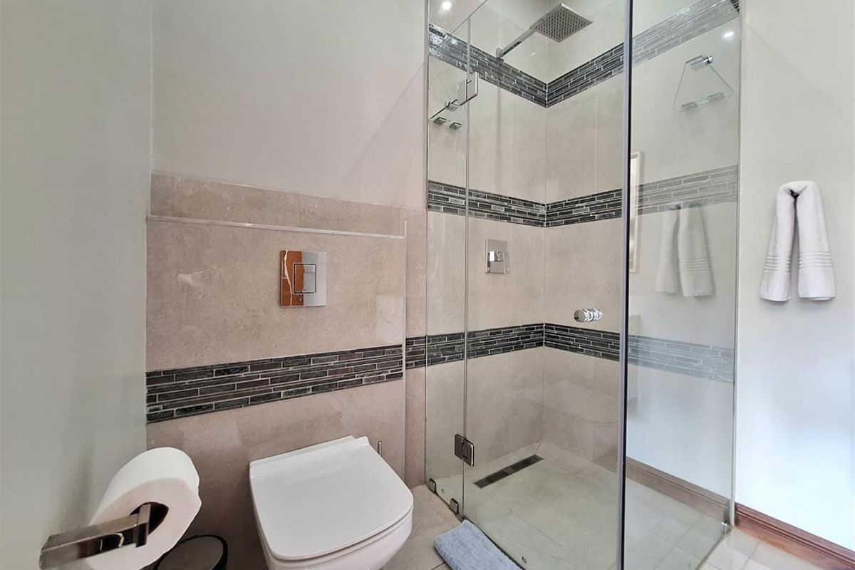 Modern bathroom featuring a frameless glass walk-in shower with a rainfall showerhead, wall-mounted toilet, and decorative mosaic tile accents.