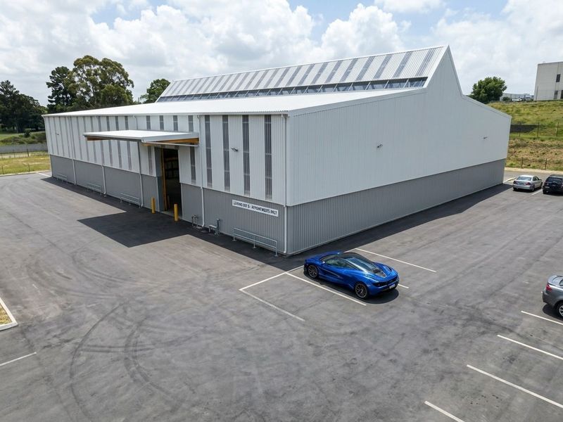 Aerial view of a modern industrial warehouse featuring metal cladding, integrated skylights, a loading bay canopy, and a paved asphalt parking area.