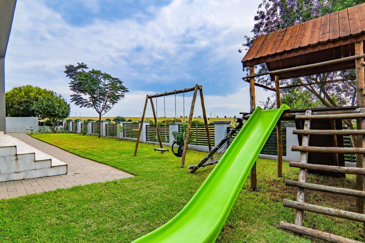 A well-maintained rear garden featuring a paved patio area, manicured lawn, perimeter fencing, and a wooden children's play structure with a slide.