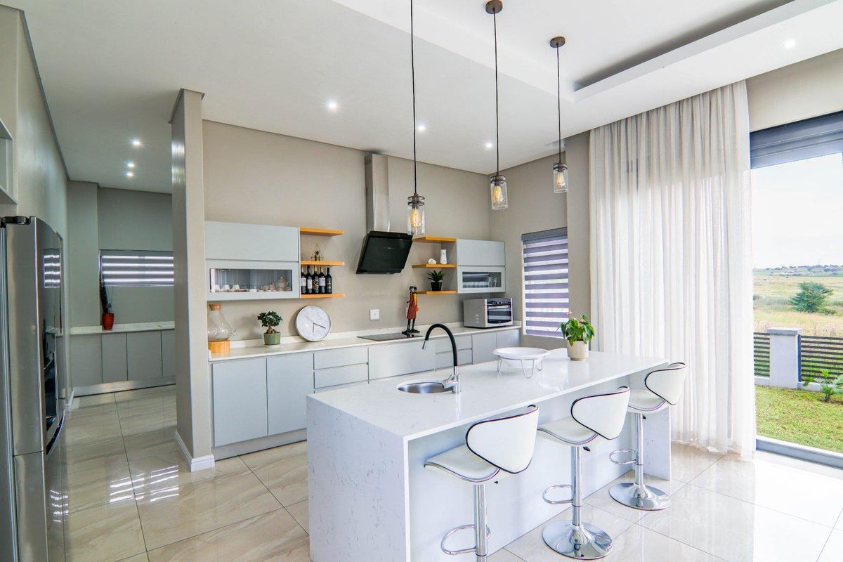 Modern open-plan kitchen featuring a central island with stone countertops, sleek cabinetry, integrated extractor fan, and direct access to the outdoor area.