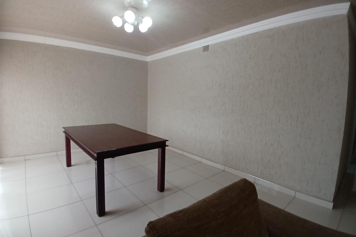 A spacious living area featuring neutral textured wallpaper, white tiled flooring, and decorative ceiling cornicing.