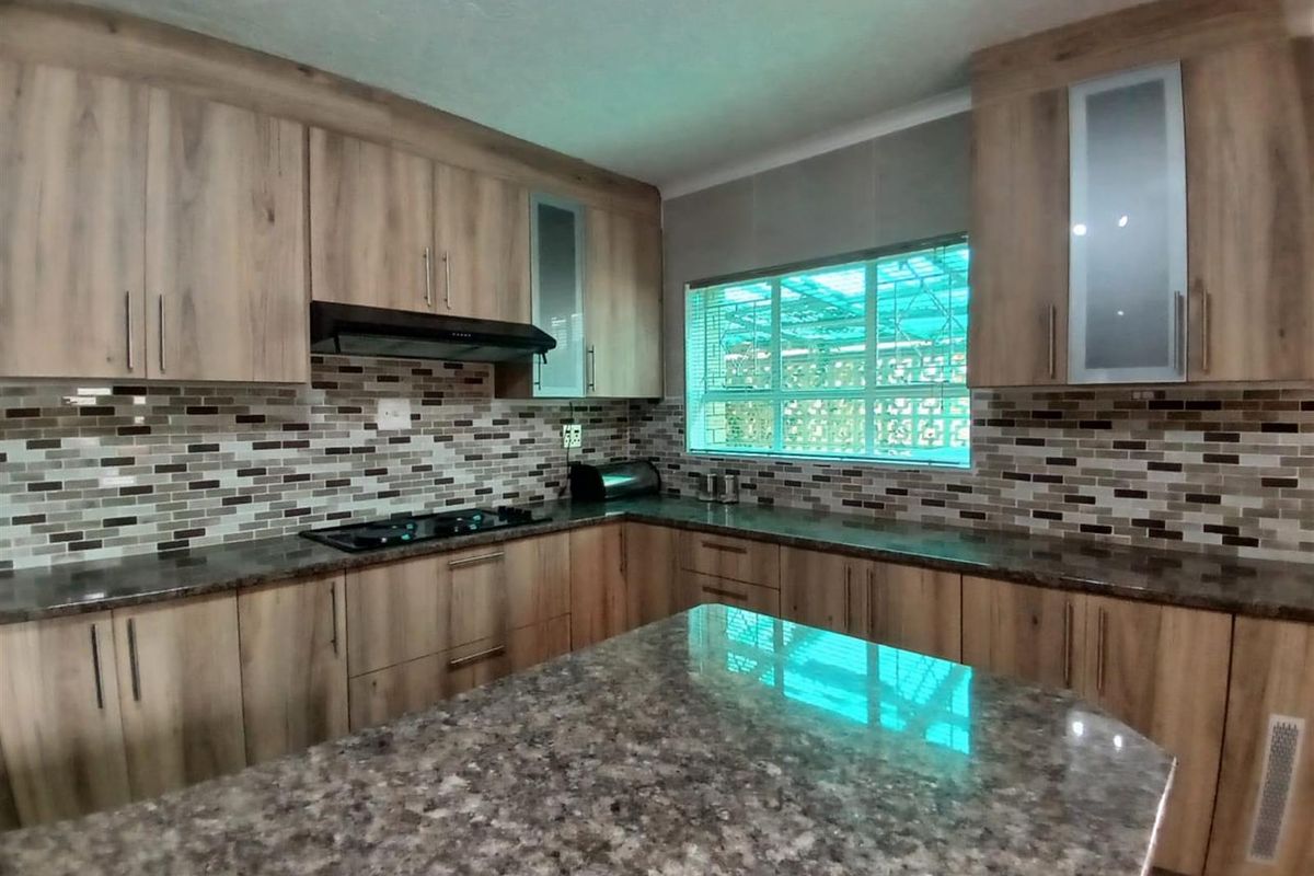 Modern kitchen featuring wood-grain cabinetry, granite countertops, a central island, and a decorative mosaic tile backsplash.