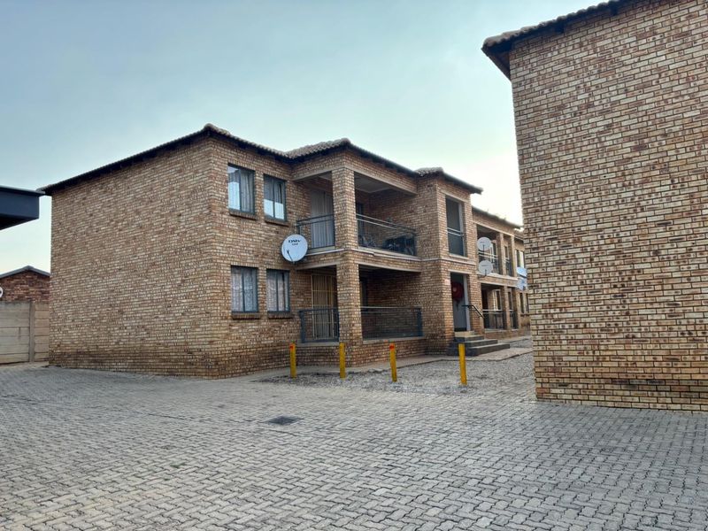 Exterior view of a multi-story apartment complex featuring face brick construction, private balconies with metal railings, and a paved driveway area.