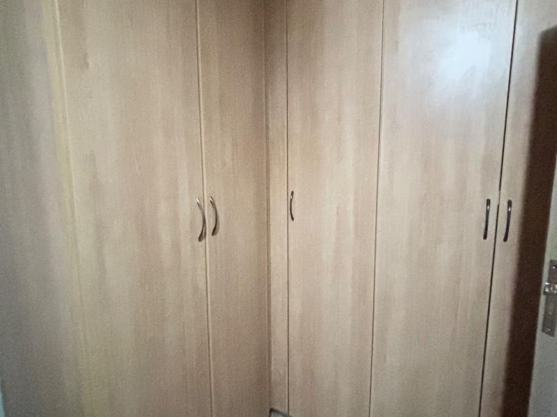 A bedroom corner featuring light wood-finish built-in cupboards and tiled flooring, offering ample storage space.