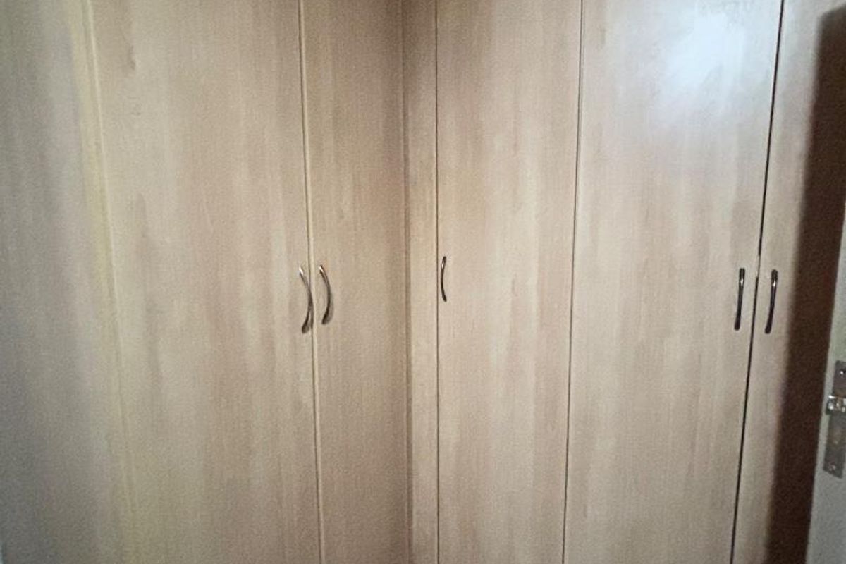 A bedroom corner featuring light wood-finish built-in cupboards and tiled flooring, offering ample storage space.