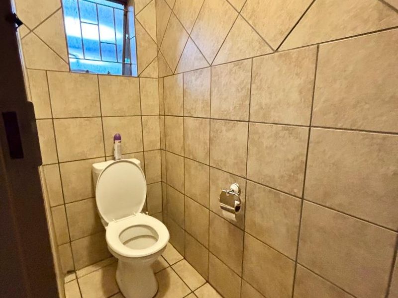 A compact, fully tiled guest bathroom featuring a standard toilet and a small window with security bars.
