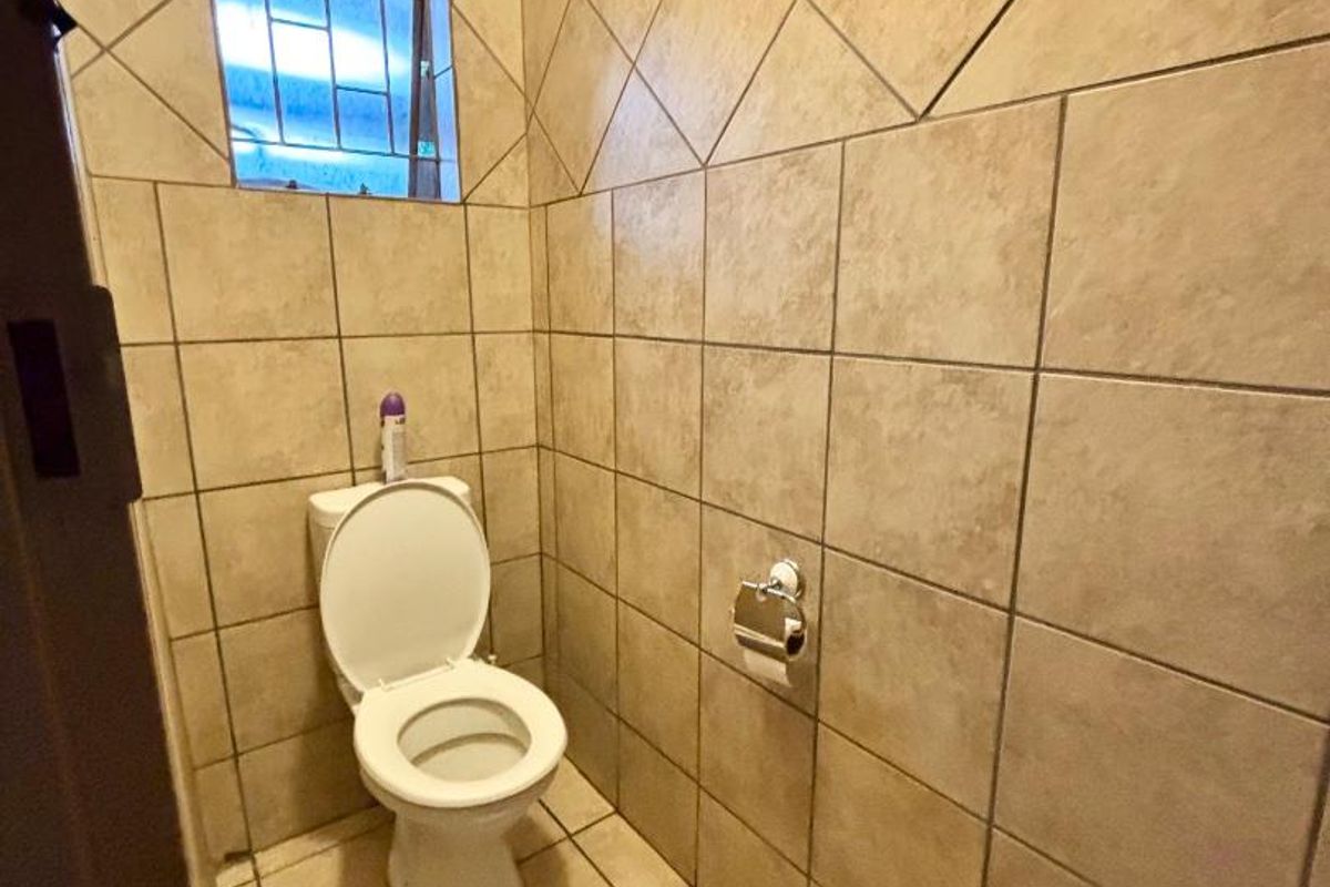 A compact, fully tiled guest bathroom featuring a standard toilet and a small window with security bars.