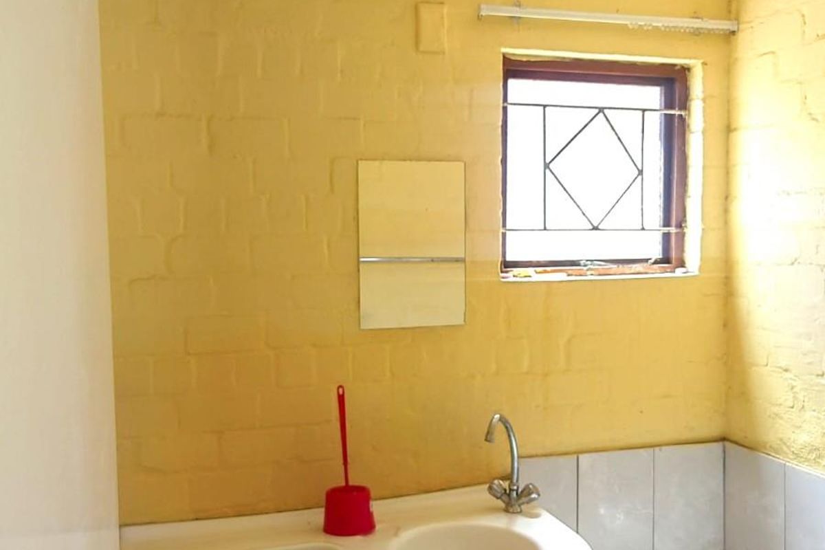 A compact bathroom featuring a built-in vanity, integrated toilet, and bathtub with a window and security bars.