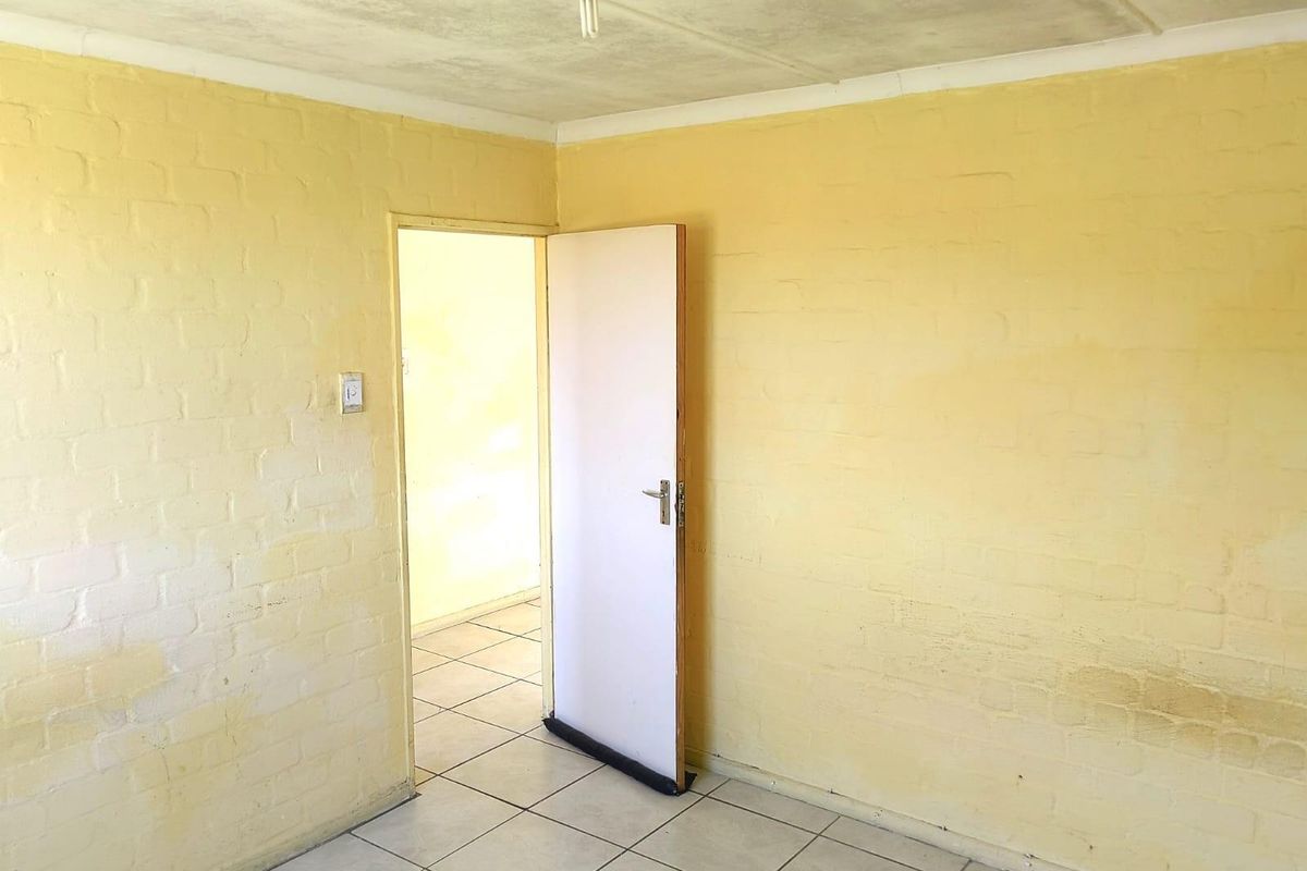 An empty room featuring tiled flooring and painted brick walls, showing signs of wear and requiring cosmetic updates.