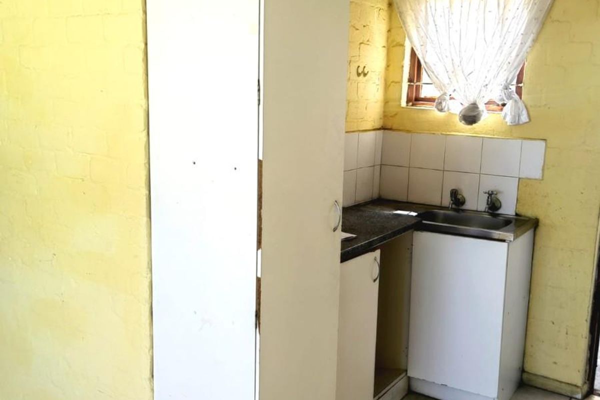 A compact kitchen area featuring a single sink, built-in cabinetry, and tiled flooring, requiring cosmetic updates to modernize the space.