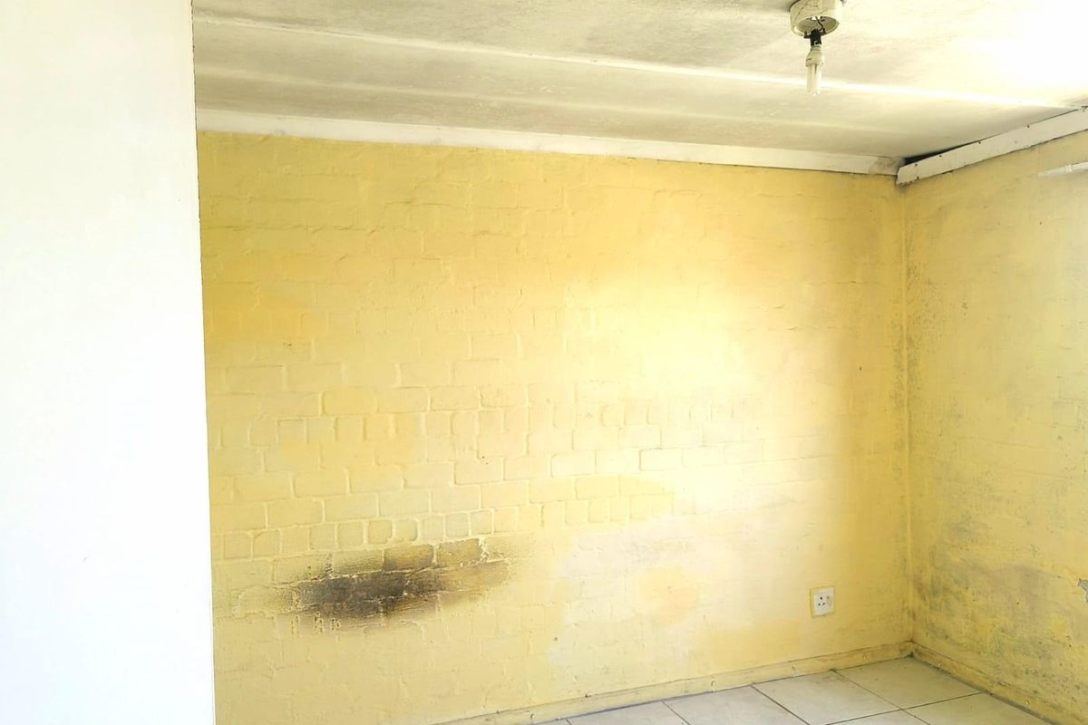An empty room featuring yellow painted brick walls, tiled flooring, and a basic ceiling light fixture, requiring cosmetic updates and repairs.