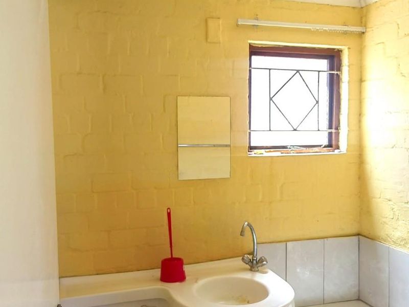 A compact bathroom featuring a built-in vanity, integrated toilet, and bathtub with a window and security bars.