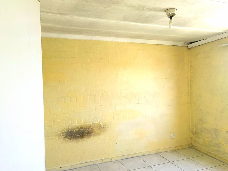 An empty room featuring yellow painted brick walls, tiled flooring, and a basic ceiling light fixture, requiring cosmetic updates and repairs.